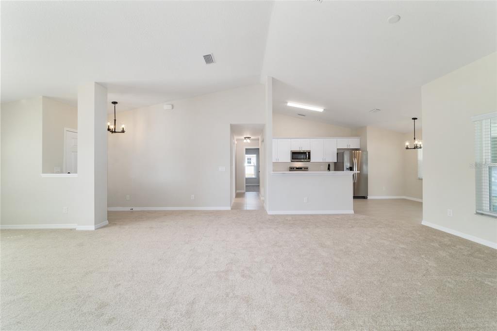 A spacious living area with beige carpet leads to a kitchen with white cabinets — 1769 NE 161ST PLACE, CITRA, FL