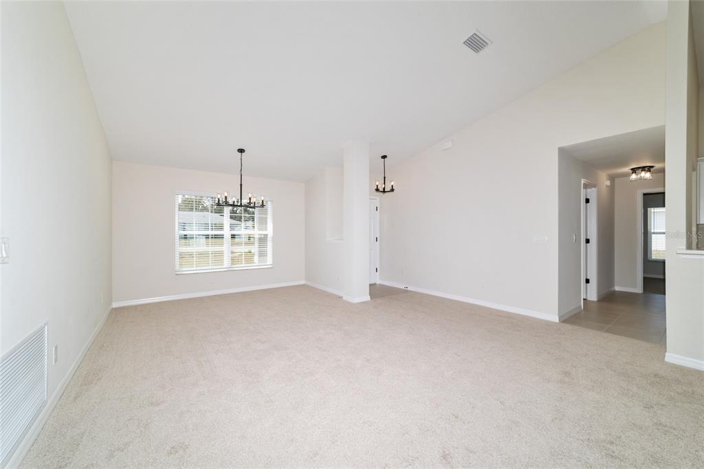 A spacious room with beige carpet, vaulted ceilings, two chandeliers, and a window — 1769 NE 161ST PLACE, CITRA, FL