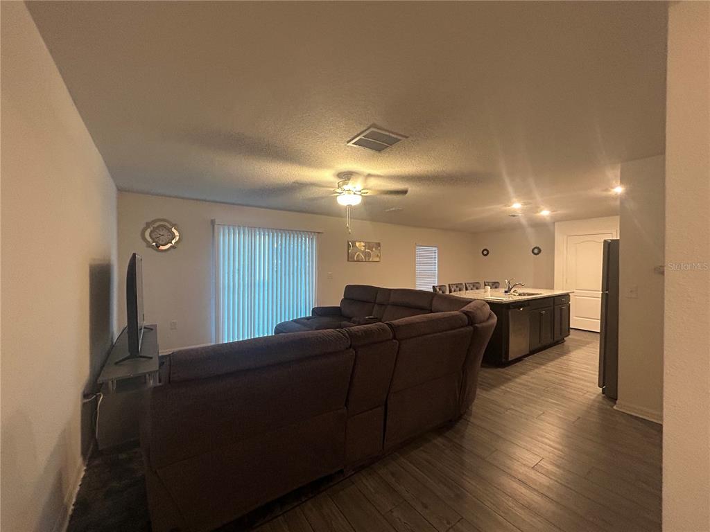 An open-concept living room features a large sectional sofa, wood-look flooring, and a kitchen island — 1303 CONGO COURT, POINCIANA, FL