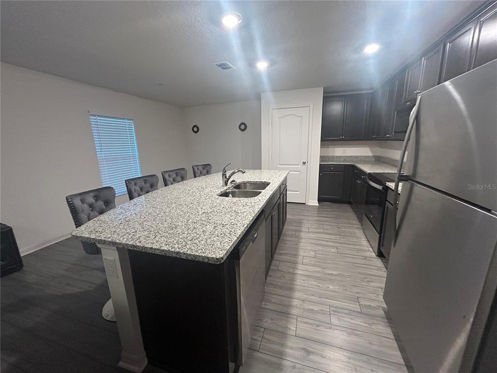 A kitchen features dark cabinets, a granite-topped island with a sink, and stainless steel appliances — 1303 CONGO COURT, POINCIANA, FL