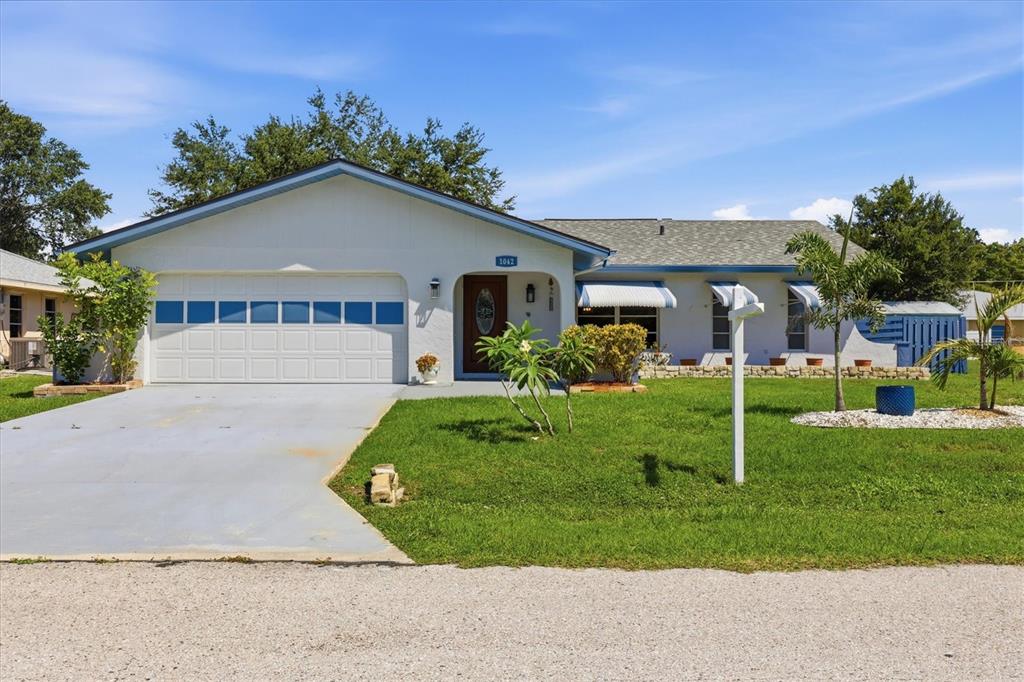 A single-story white house with a garage, blue trim, and a front lawn — 1042 MALAY TERRACE NW, PORT CHARLOTTE, FL