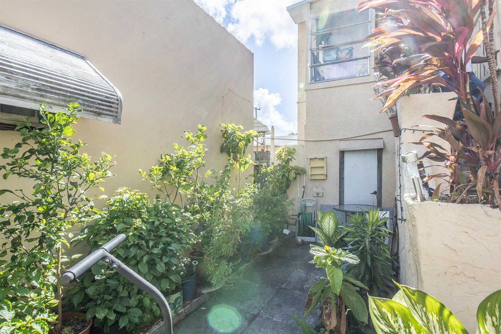 A narrow outdoor walkway between two buildings features potted plants and a concrete path — 928 S Dixie Highway, FL 33460, FL