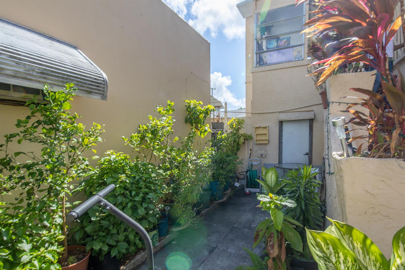 A narrow outdoor walkway between two buildings features potted plants and a small white door — 928 S Dixie Highway, FL 33460, FL