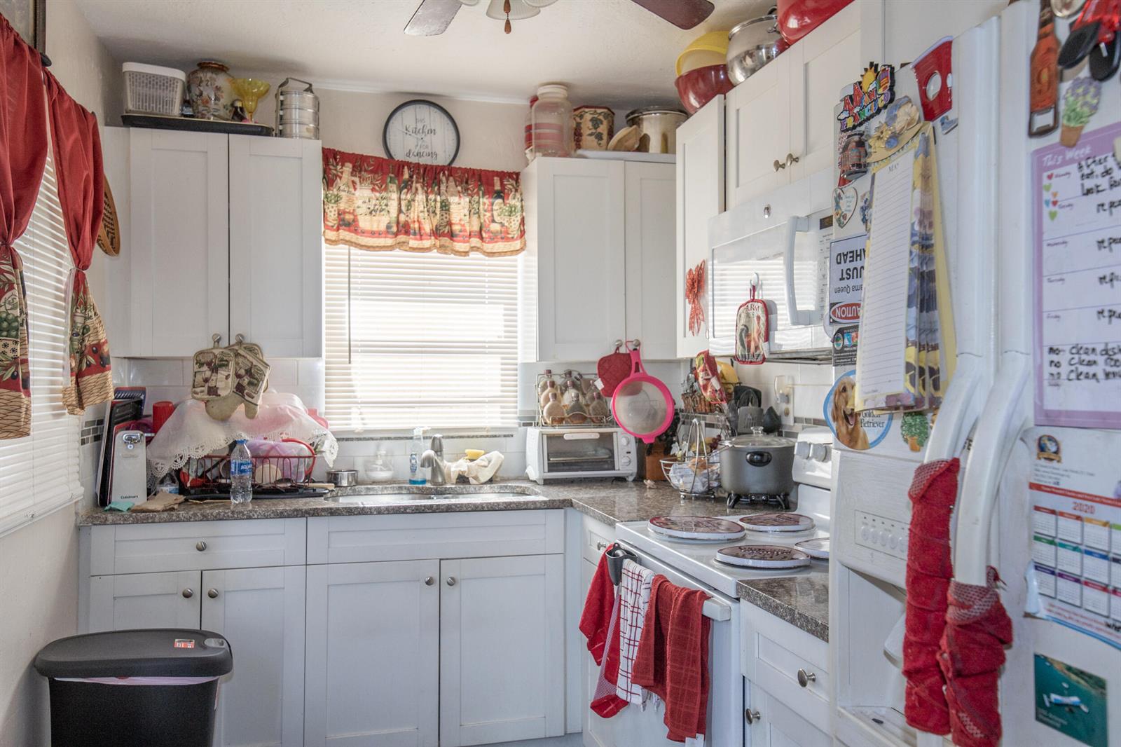 A small kitchen features white cabinets, granite countertops, a stainless steel sink, and white appliances — 928 S Dixie Highway, FL 33460, FL