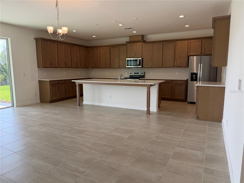A kitchen with brown cabinets, a central island, stainless steel appliances, and tile flooring — 756 FARFIELDS STREET, DELAND, FL