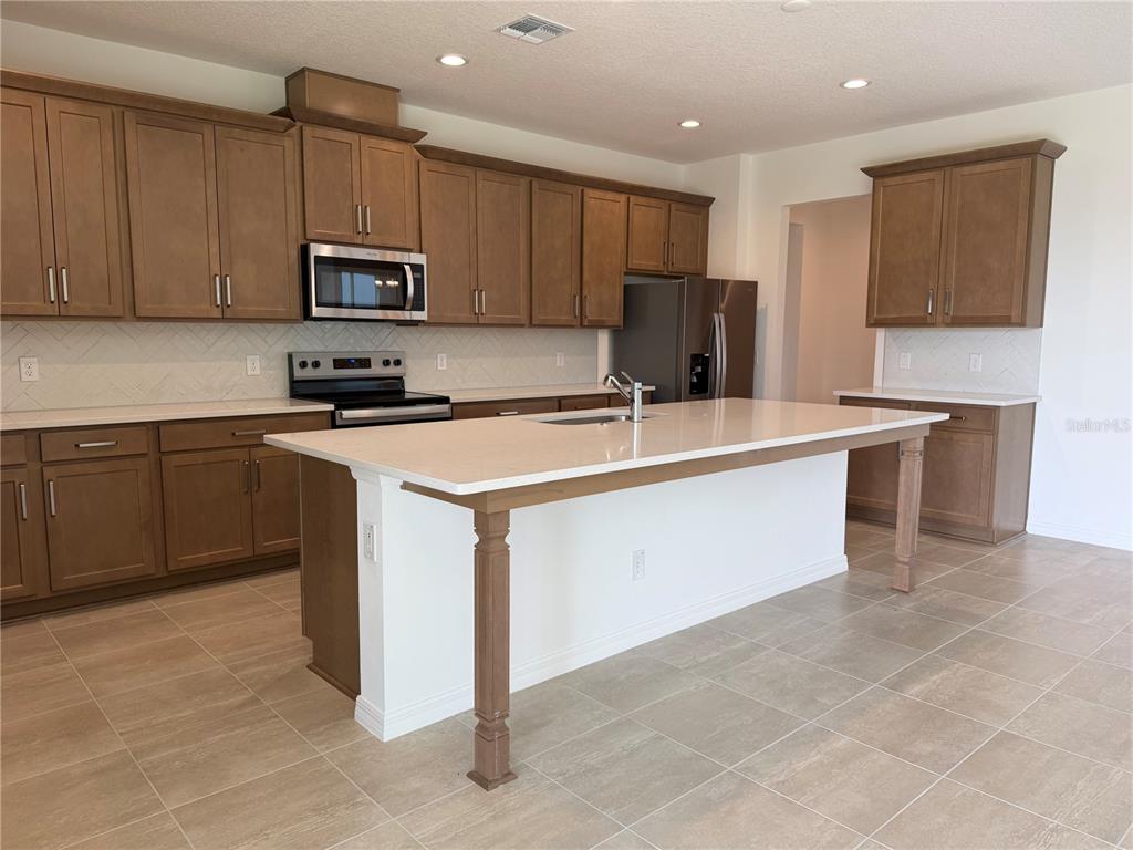 A kitchen features brown wooden cabinets, a large white island, and light-colored tile flooring — 756 FARFIELDS STREET, DELAND, FL