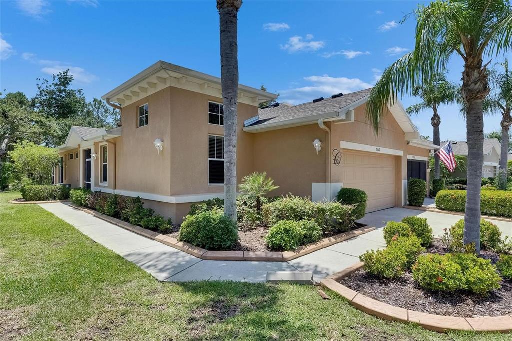 A tan stucco house with a two-car garage and a palm tree in the front yard — 2068 SIFIELD GREENS WAY, SUN CITY CENTER, FL