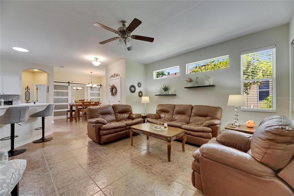 A living room with brown leather furniture, tile flooring, and a dining area in the background — 2068 SIFIELD GREENS WAY, SUN CITY CENTER, FL
