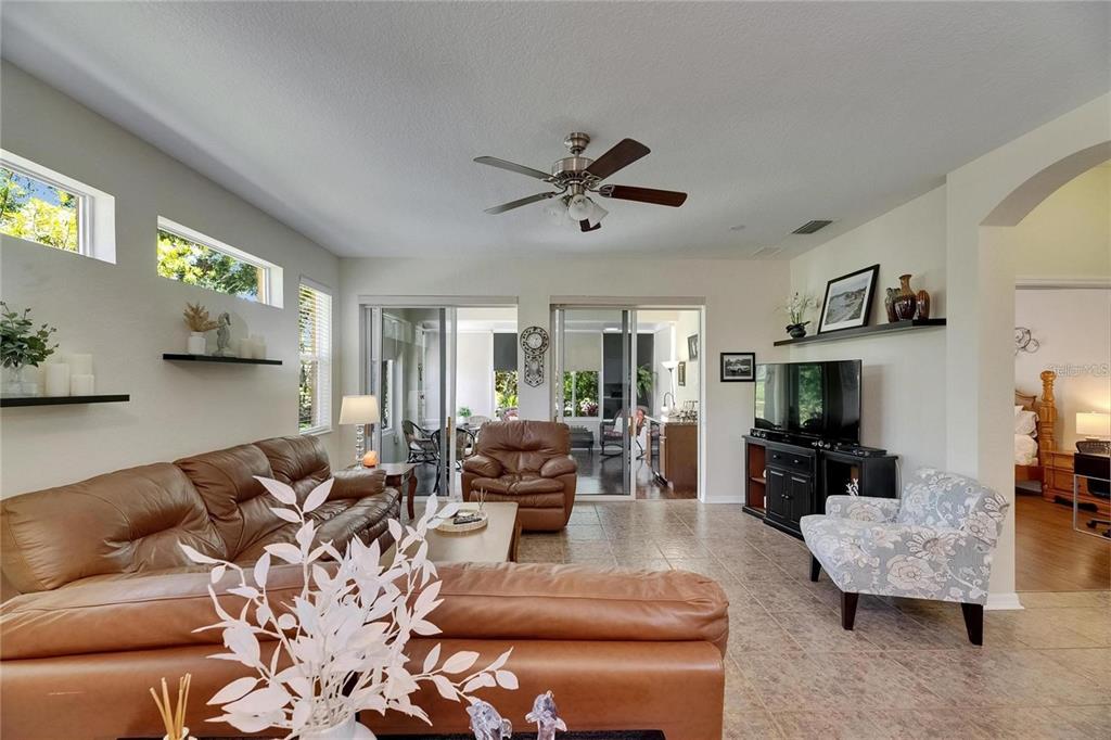 A living room features a leather sofa, patterned armchair, ceiling fan, and sliding glass doors — 2068 SIFIELD GREENS WAY, SUN CITY CENTER, FL