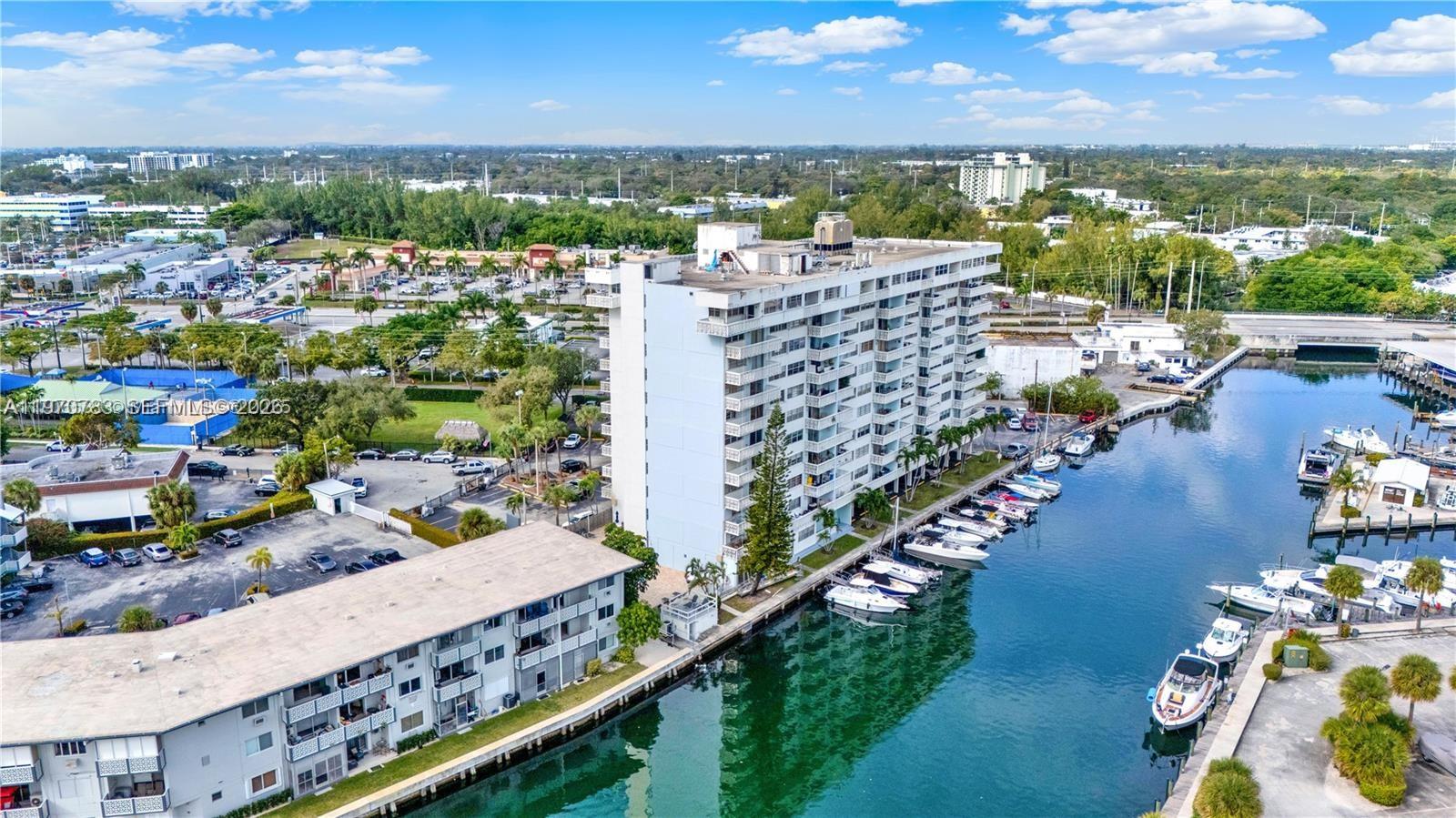 An aerial view shows a tall residential building situated along a canal with docked boats — 13155 Ixora Ct # 311, North Miami FL 33181, NORTH MIAMI, FL
