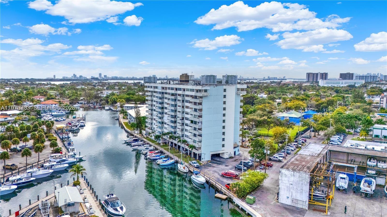 An aerial view shows a multi-story apartment building situated along a canal filled with boats — 13155 Ixora Ct # 311, North Miami FL 33181, NORTH MIAMI, FL
