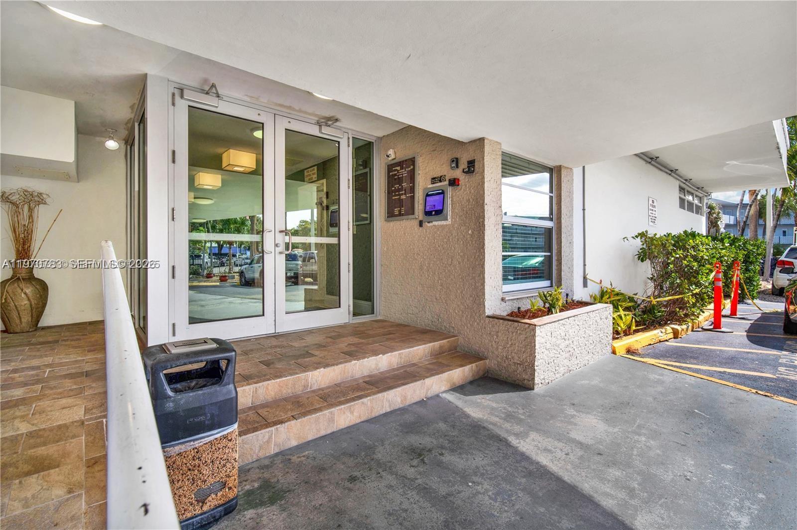 The exterior entrance features glass double doors, tiled steps, and a concrete parking area — 13155 Ixora Ct # 311, North Miami FL 33181, NORTH MIAMI, FL