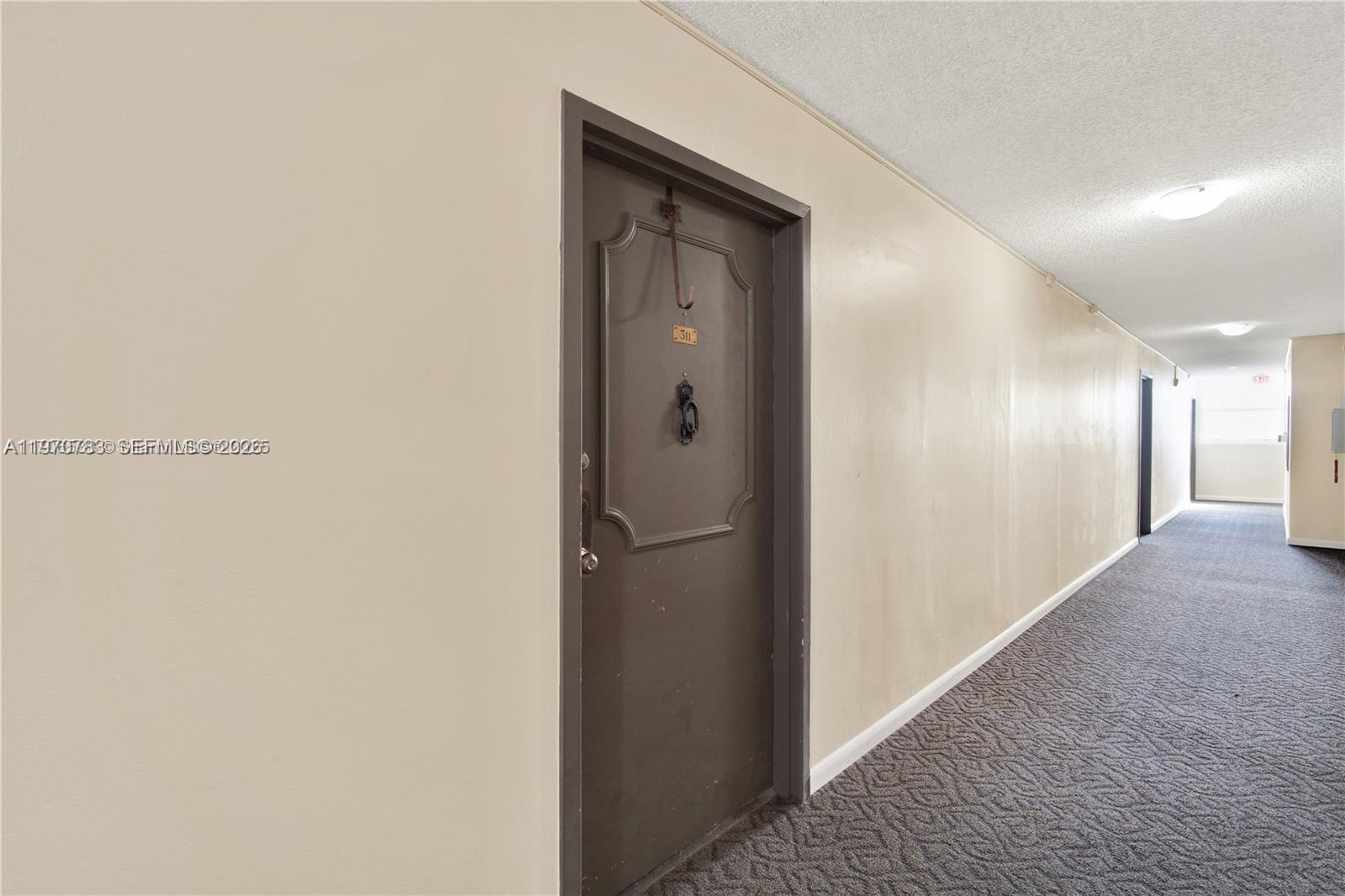 A hallway with beige walls, gray carpet, and a dark brown door labeled 311 — 13155 Ixora Ct # 311, North Miami FL 33181, NORTH MIAMI, FL