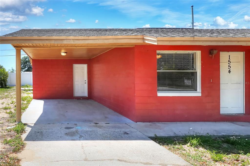 A red concrete block house features a front carport, a single window, and a white door — 1554 SARAH STREET, LAKE WALES, FL