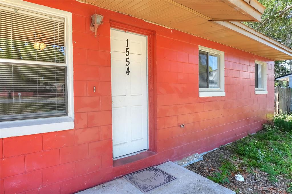The exterior of a house features bright orange concrete block walls and a white door — 1554 SARAH STREET, LAKE WALES, FL
