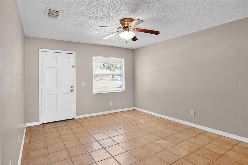An empty room with beige walls, tan tile flooring, a ceiling fan, and a white door — 1554 SARAH STREET, LAKE WALES, FL