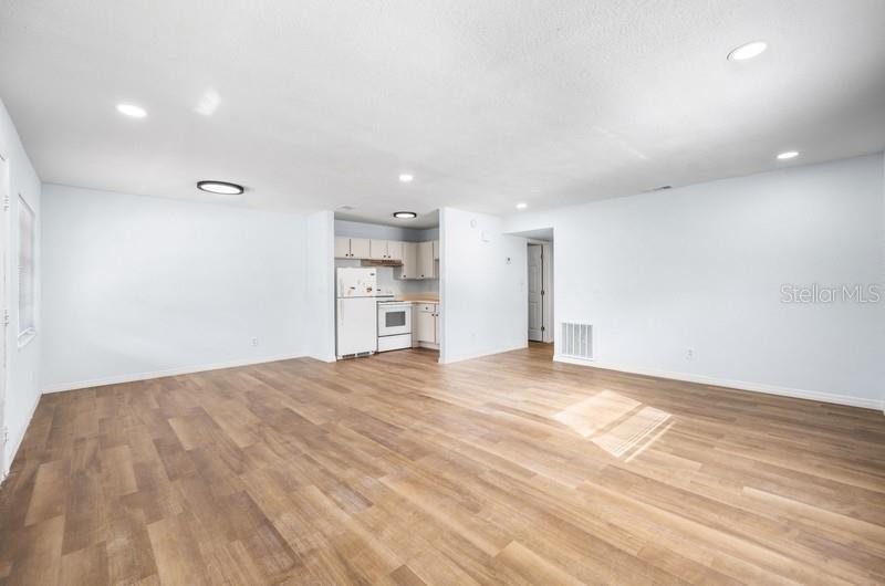 A spacious room with light-colored walls, wood-look flooring, and an open kitchen area — 1132 AUBURN STREET, CLEARWATER, FL
