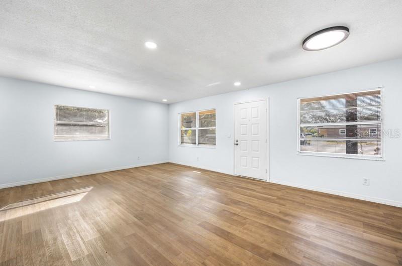 An empty room with light-colored walls, wood-look flooring, a white door, and three windows — 1132 AUBURN STREET, CLEARWATER, FL