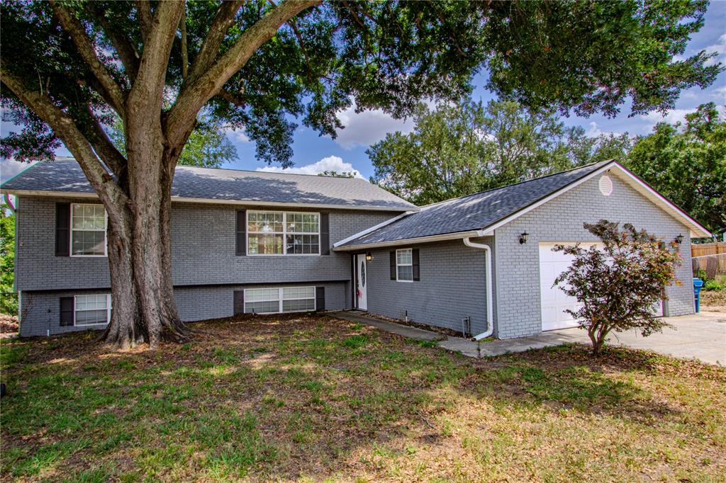 A gray brick split-level house with a large tree and an attached garage — 2614 CREST DRIVE, HAINES CITY, FL