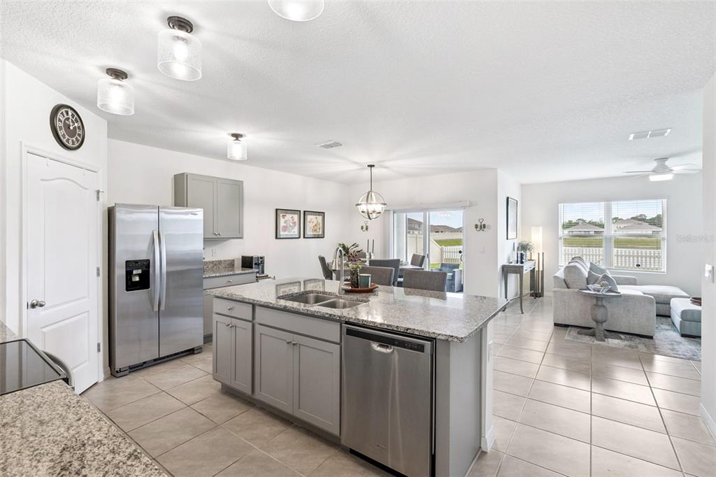 A kitchen with gray cabinets and granite countertops opens to a dining area and living room — 5634 WINONA DRIVE, ST CLOUD, FL