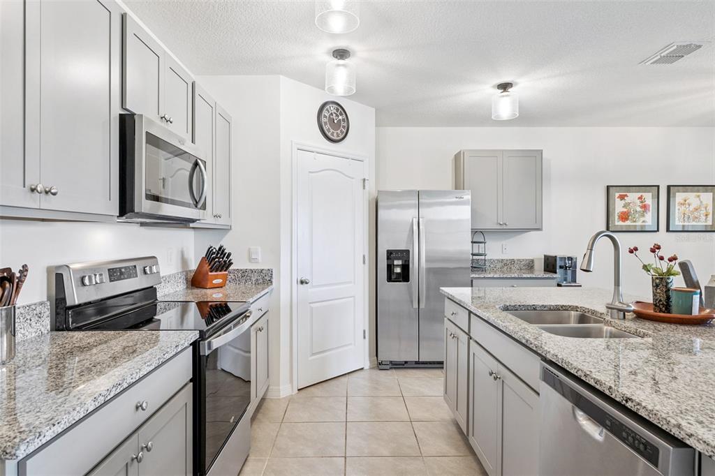 A kitchen features gray cabinets, granite countertops, stainless steel appliances, and a central island — 5634 WINONA DRIVE, ST CLOUD, FL