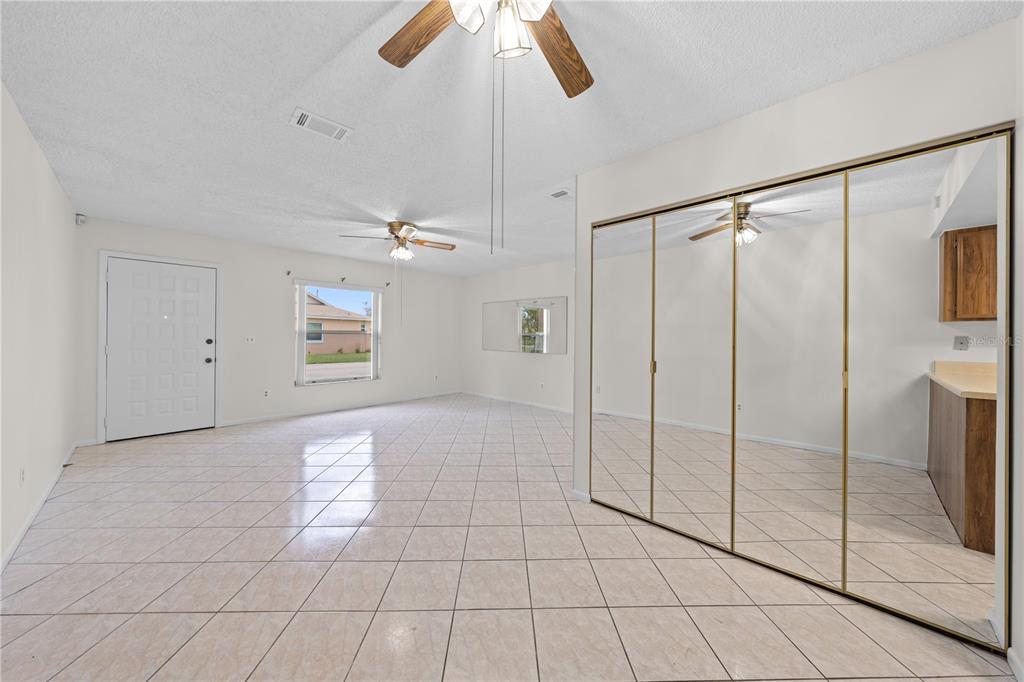 A living room with white tile floors, two ceiling fans, and large mirrored closet doors — 59 E COUNTRY COVE, KISSIMMEE, FL