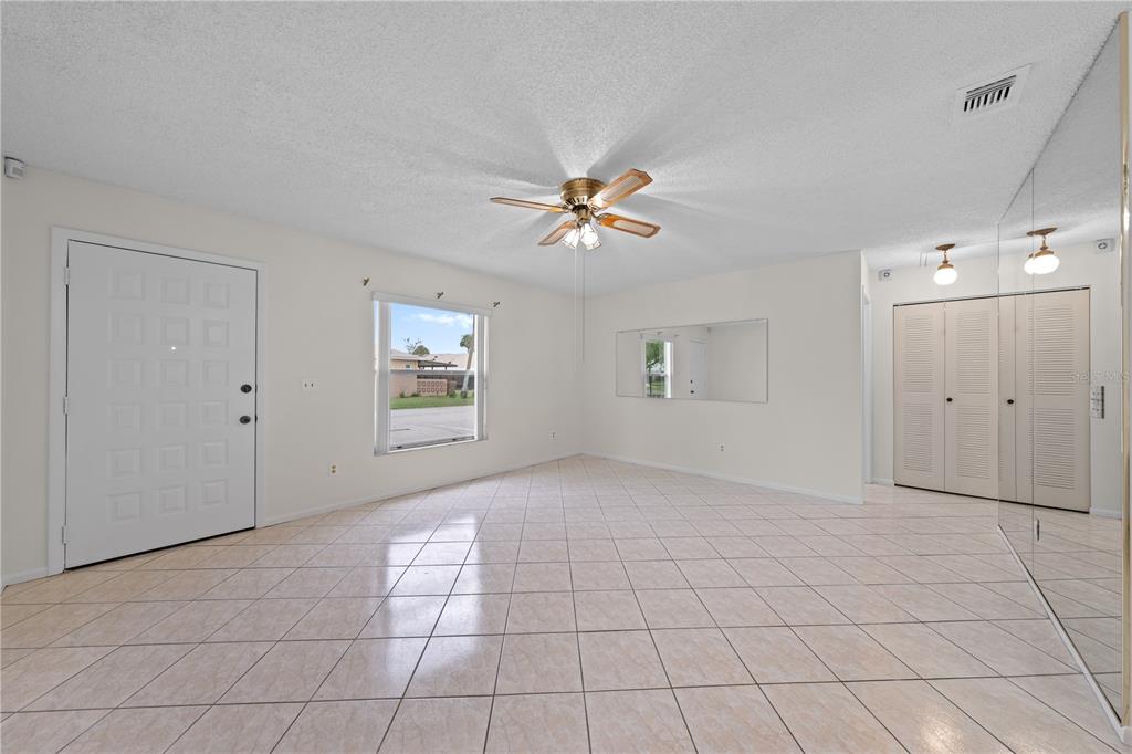 A bright living room features light-colored tile flooring, a ceiling fan, and mirrored closet doors — 59 E COUNTRY COVE, KISSIMMEE, FL