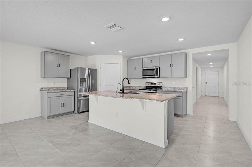 A kitchen features gray cabinets, granite countertops, a central island, and light-colored tile flooring — 17319 WHEATBERRY BOULEVARD, PARRISH, FL