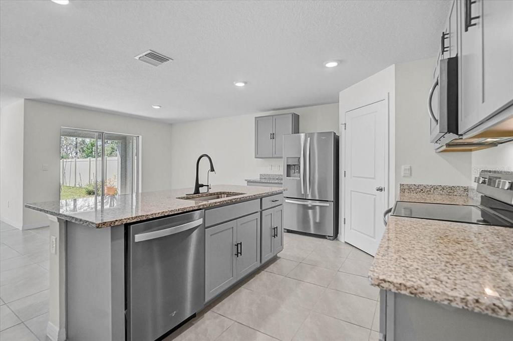 A kitchen with gray cabinets, granite countertops, stainless steel appliances, and a center island — 17319 WHEATBERRY BOULEVARD, PARRISH, FL