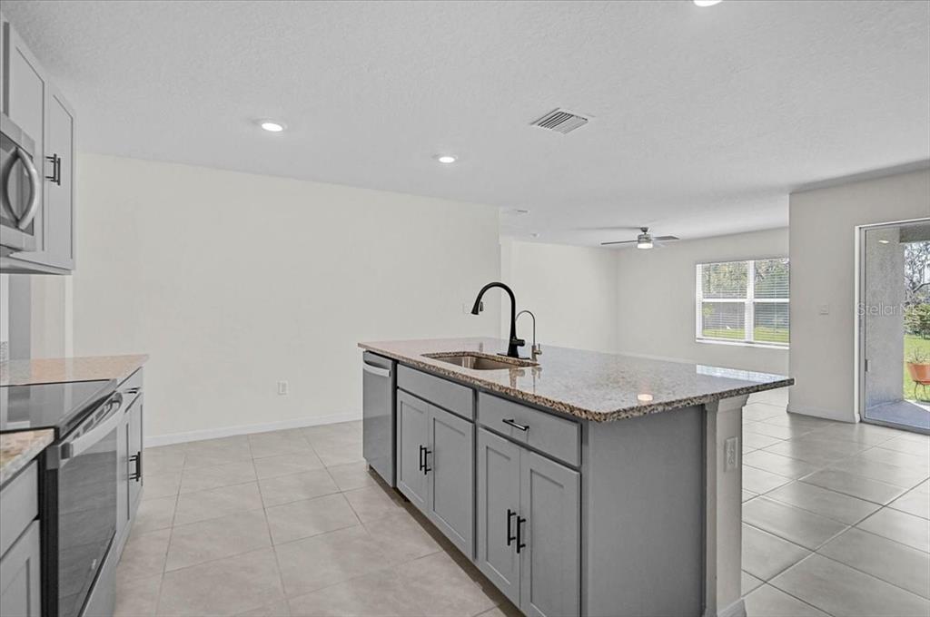 A kitchen features a gray island with a granite countertop and a stainless steel sink — 17319 WHEATBERRY BOULEVARD, PARRISH, FL