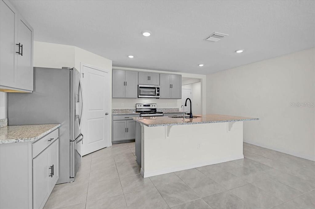 A kitchen features gray cabinets, granite countertops, a center island, and stainless steel appliances — 17319 WHEATBERRY BOULEVARD, PARRISH, FL