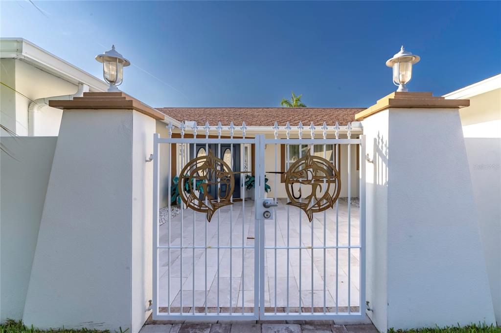 A white metal gate with decorative fish cutouts stands between two stucco pillars with lamps — 320 HARBOR PASSAGE, CLEARWATER BEACH, FL
