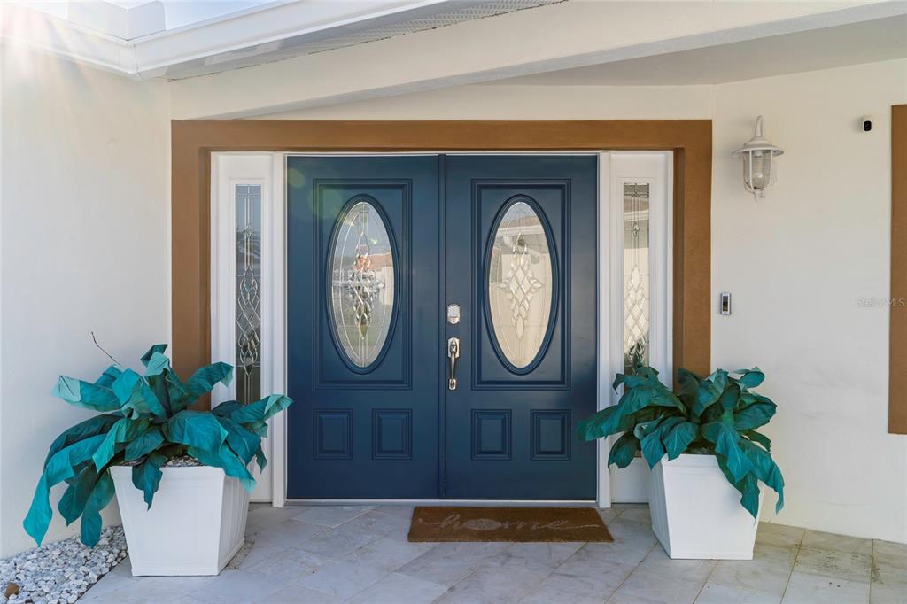 A blue double front door with glass inserts is flanked by two potted plants — 320 HARBOR PASSAGE, CLEARWATER BEACH, FL
