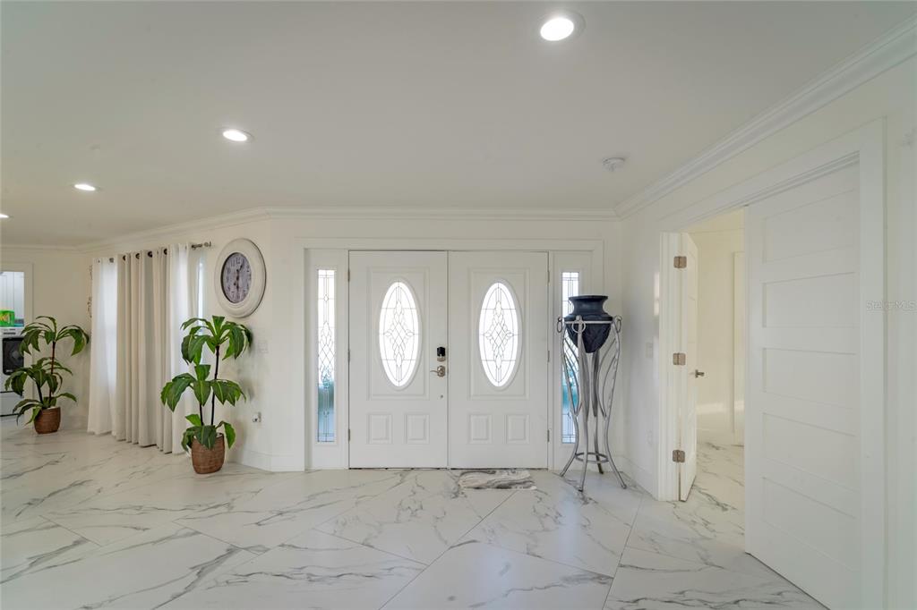 A bright entryway features white double doors, marble-patterned tile flooring, and a potted plant — 320 HARBOR PASSAGE, CLEARWATER BEACH, FL