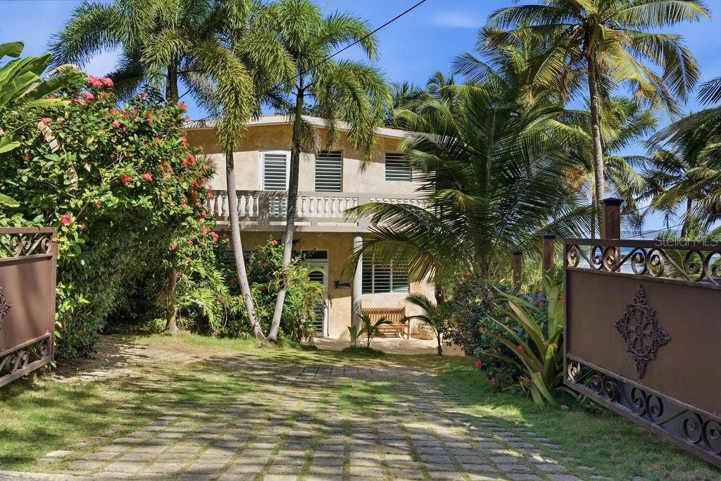 A two-story house with a paved driveway, palm trees, and a decorative metal gate — 26 BARRIO PUNTAS SANDY BEACH, RINCON, PR