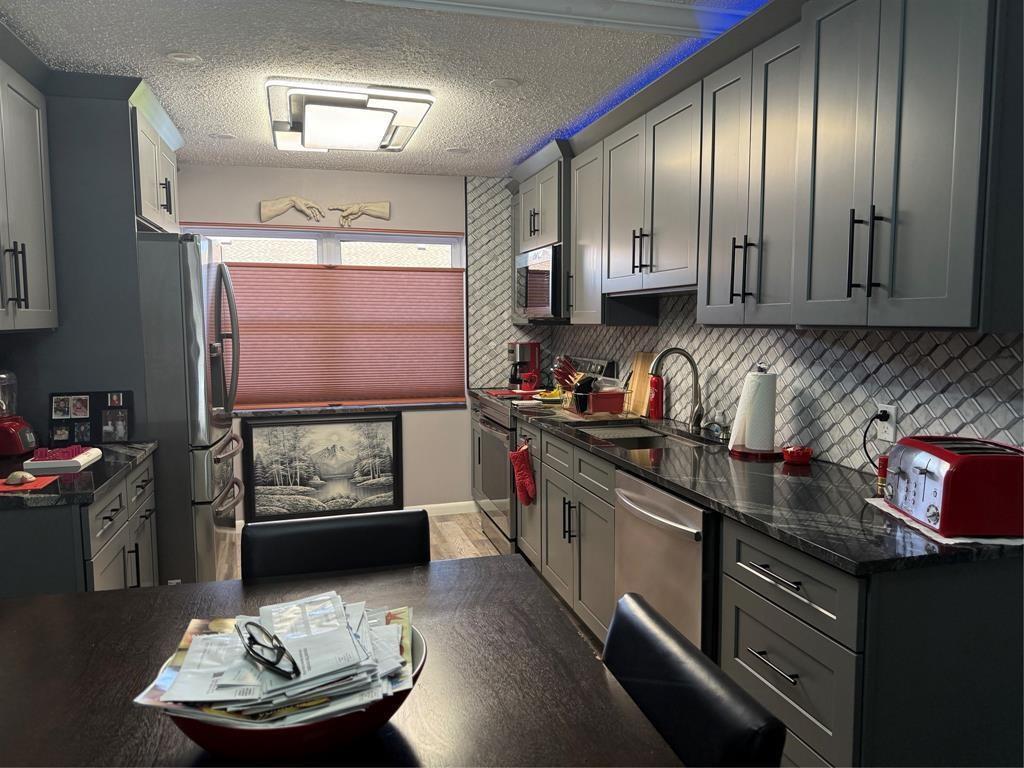 A kitchen features gray cabinets, dark countertops, a patterned backsplash, and a dining table — 25 SE 13th Street # B2, Boca Raton FL 33432, BOCA RATON, FL