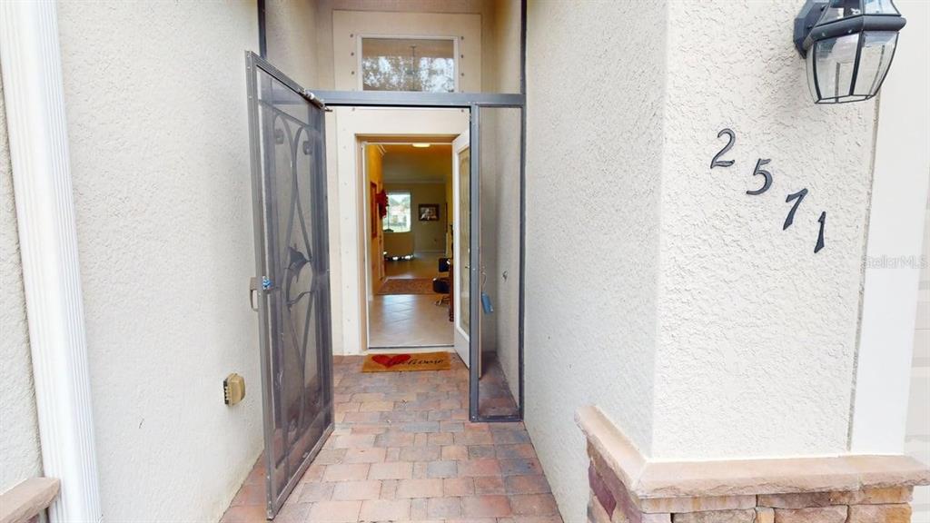 An exterior entryway features a paved floor, a decorative screen door, and house numbers — 2571 LAURENTINA LANE, CAPE CORAL, FL