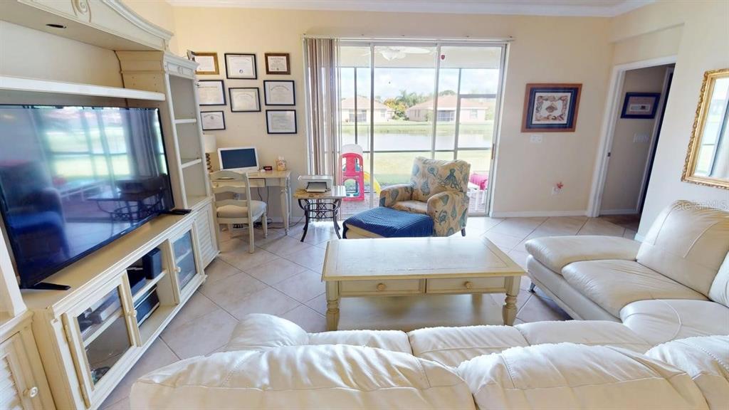 A living room features a white entertainment center, a white sofa, and a sliding glass door — 2571 LAURENTINA LANE, CAPE CORAL, FL