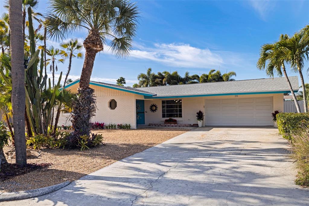 A single-story white brick house with a teal trim and a palm-filled front yard — 290 1ST STREET W, TIERRA VERDE, FL