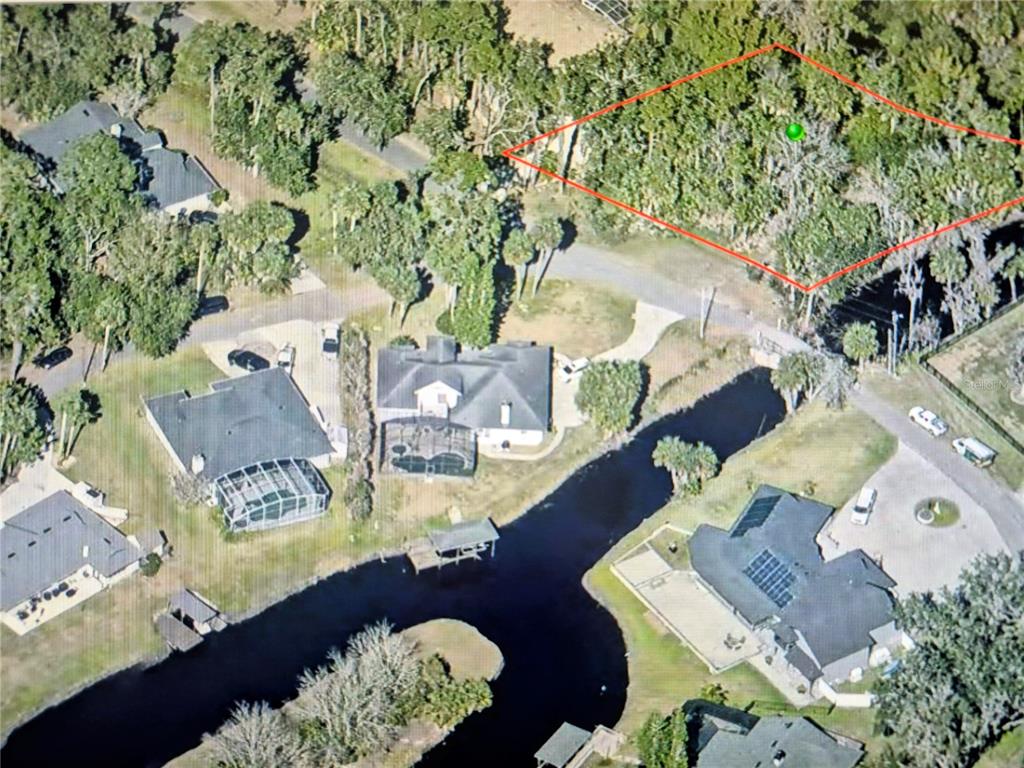 An aerial view shows a wooded, undeveloped lot outlined in red near a canal — 327 HARBOR TRAIL, DELTONA, FL