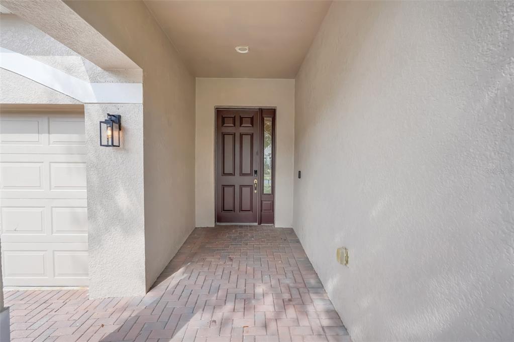 A covered entryway features a brown front door, brick pavers, and a white garage door — 2390 CALEDONIAN STREET, CLERMONT, FL