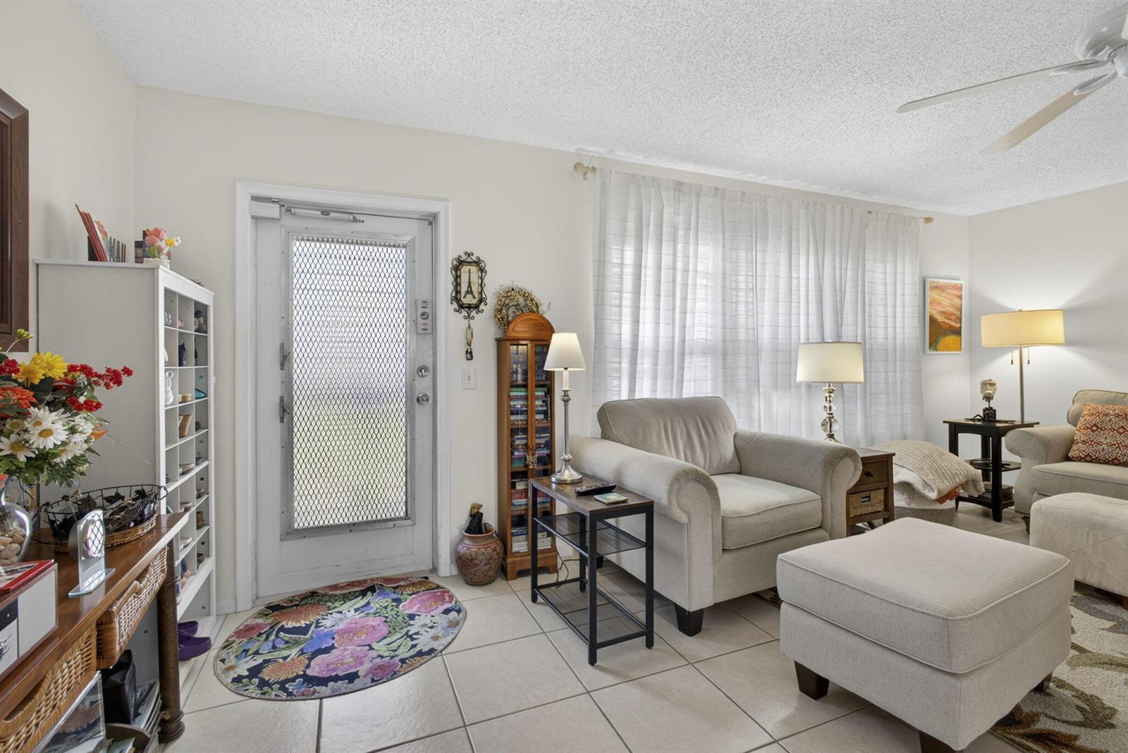 A living room features tile flooring, a white front door, an armchair, and an ottoman — 308 Greenbrier A, West Palm Beach FL 33417, WEST PALM BEACH, FL