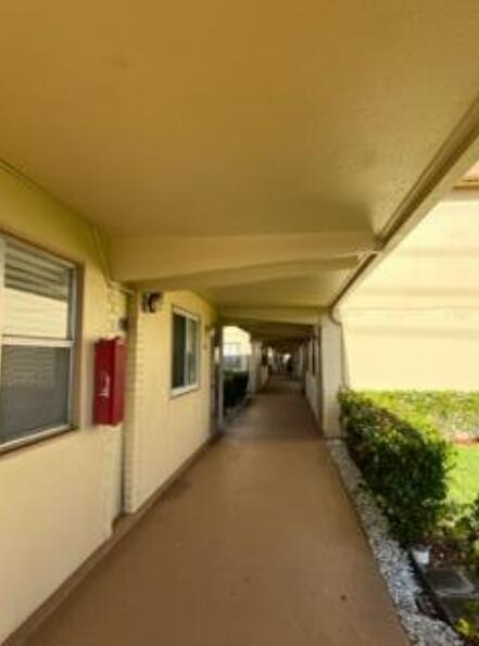An outdoor covered walkway runs along the side of a beige building with a fire extinguisher — 193 Saxony E, Delray Beach FL 33446, DELRAY BEACH, FL
