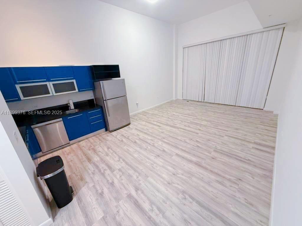 A kitchen with blue cabinets and stainless steel appliances sits in an open-plan room — 253 NE 2nd St # 226, Miami FL 33132, MIAMI, FL