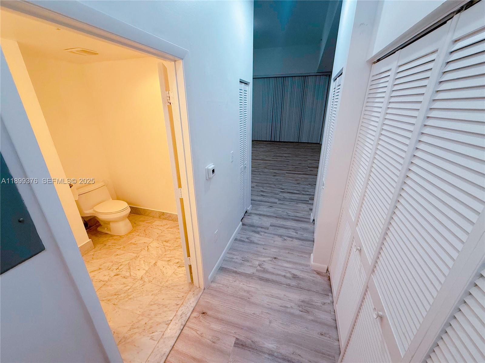 A hallway with wood-look flooring leads to a bathroom with a toilet and tiled floor — 253 NE 2nd St # 226, Miami FL 33132, MIAMI, FL