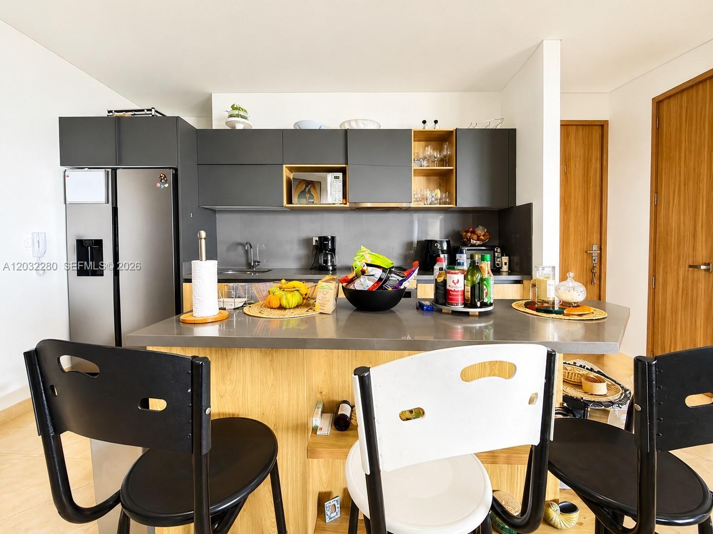 A modern kitchen features dark gray cabinets, a stainless steel refrigerator, and a wooden island — 9  6 108 # 601, At Puerto Col, At