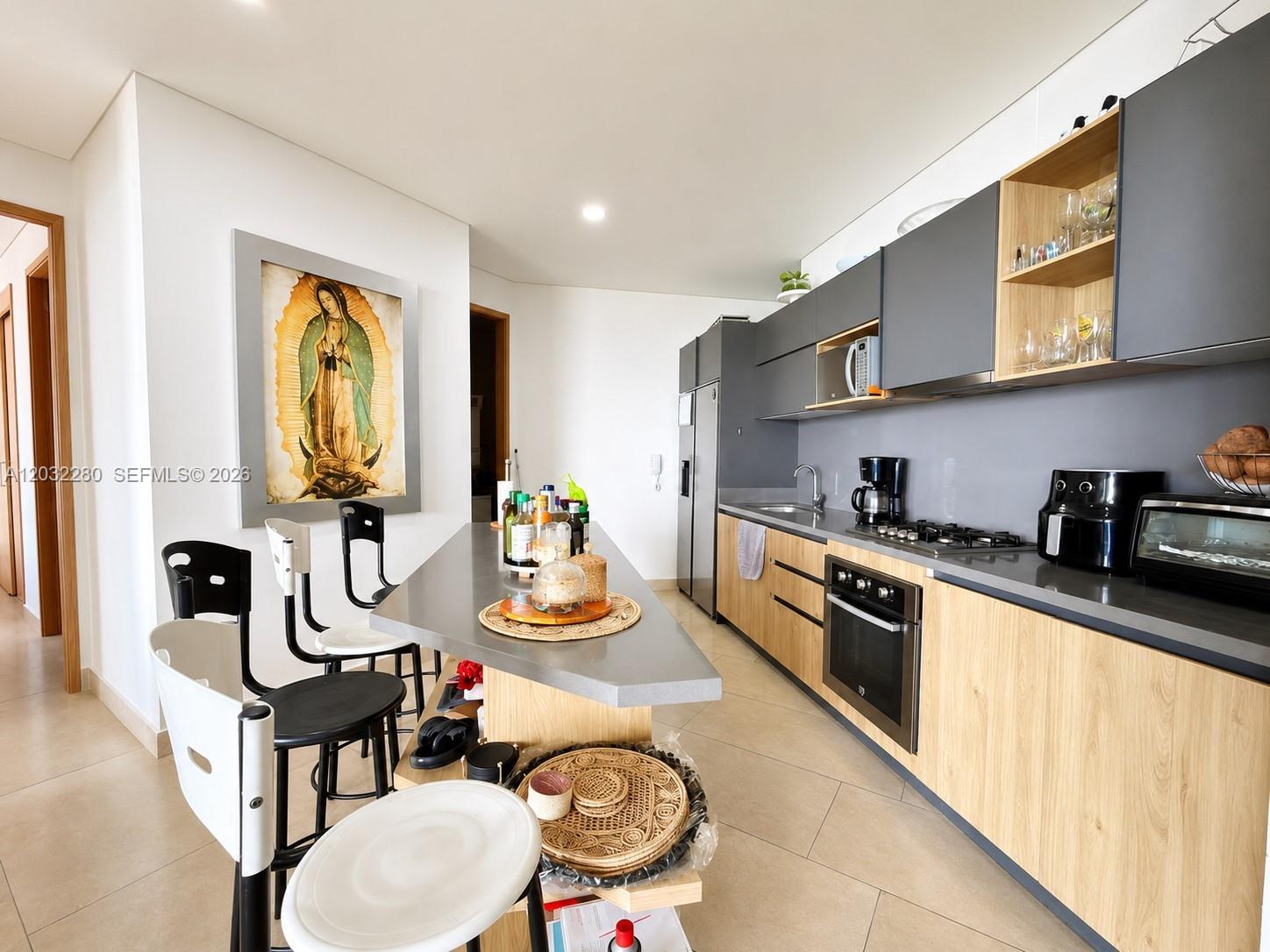 A modern kitchen features light wood cabinets, gray countertops, and a central breakfast bar — 9  6 108 # 601, At Puerto Col, At
