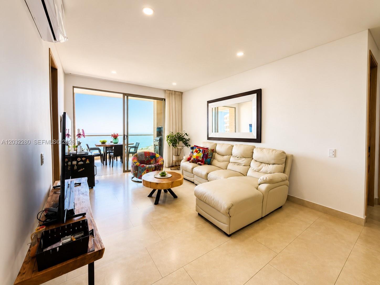A living room features a white sectional sofa, a wooden coffee table, and balcony ocean views — 9  6 108 # 601, At Puerto Col, At