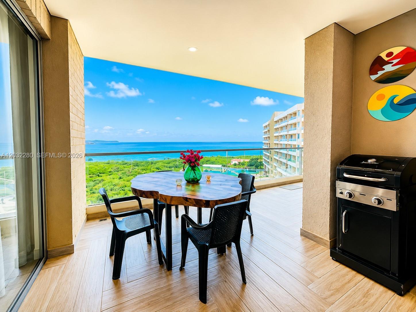 A balcony features a wooden dining table, black chairs, a grill, and ocean views — 9  6 108 # 601, At Puerto Col, At