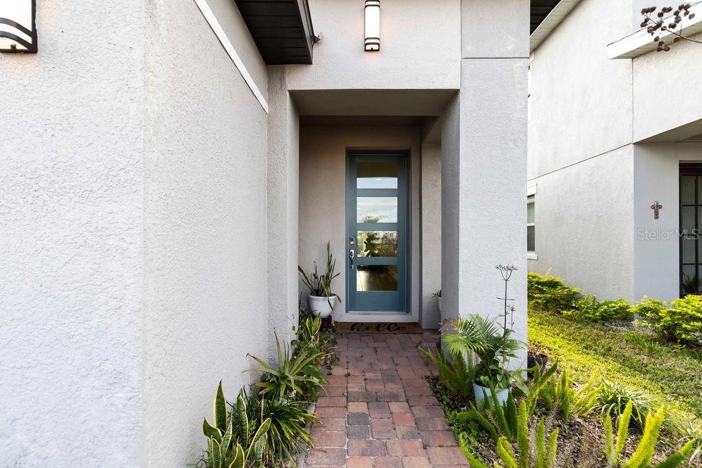 A paved walkway leads to a blue front door with glass panels under a porch — 3212 OXBOW COURT, HARMONY, FL